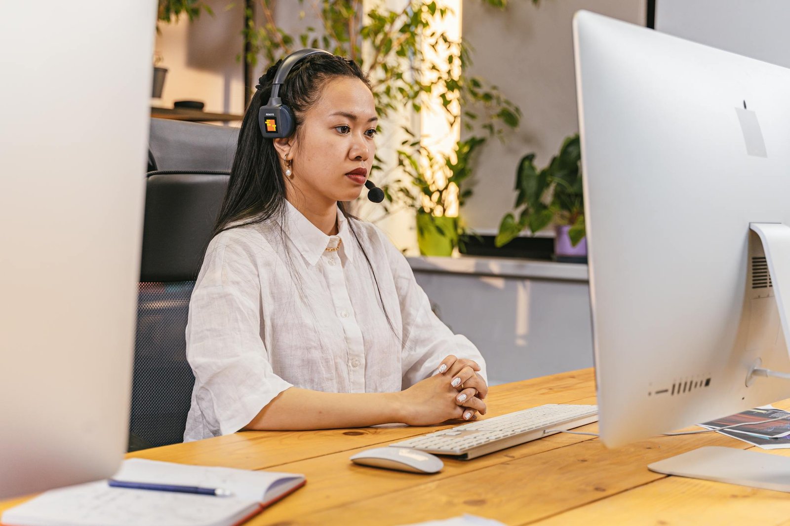 Focused woman in office wearing headset, working at a desktop computer.